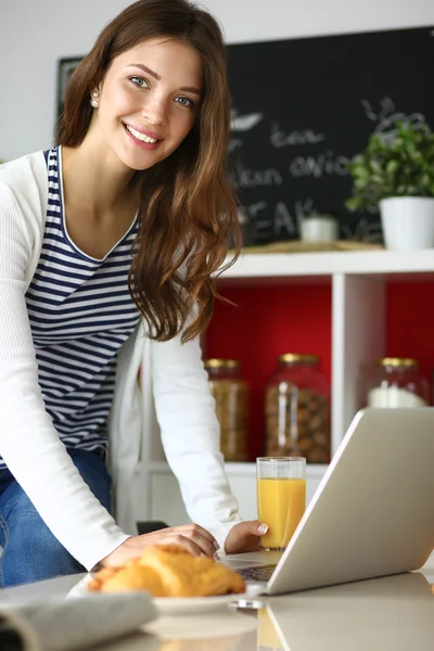 Attractive young woman using laptop and sitting in the kitchen