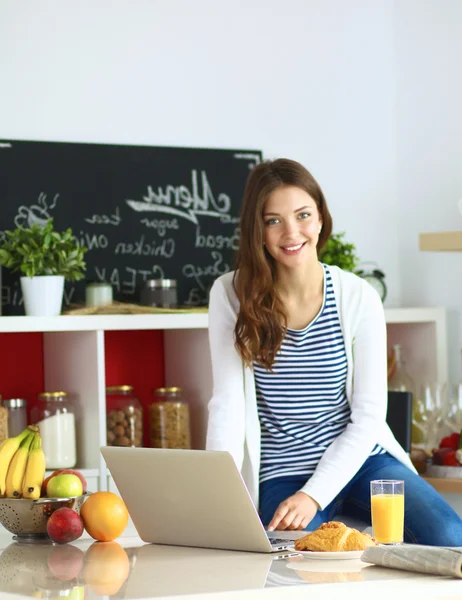 Attractive young woman using laptop and sitting in the kitchen