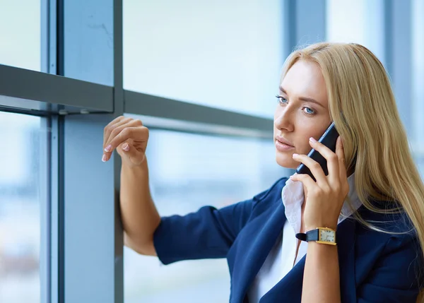 Businesswoman standing against office window talking on mobile phone
