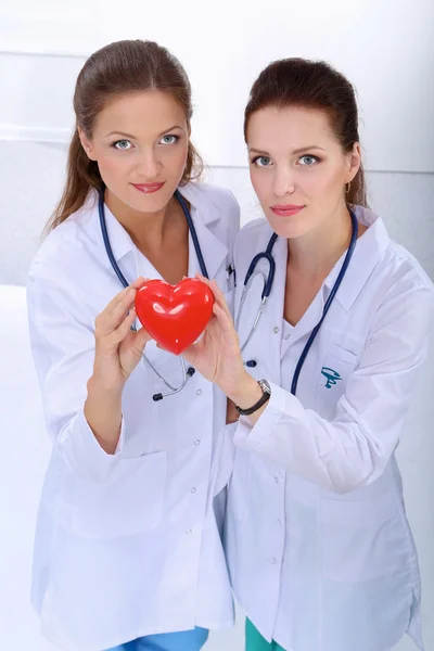 Two woman doctor holding a red heart, isolated on white background