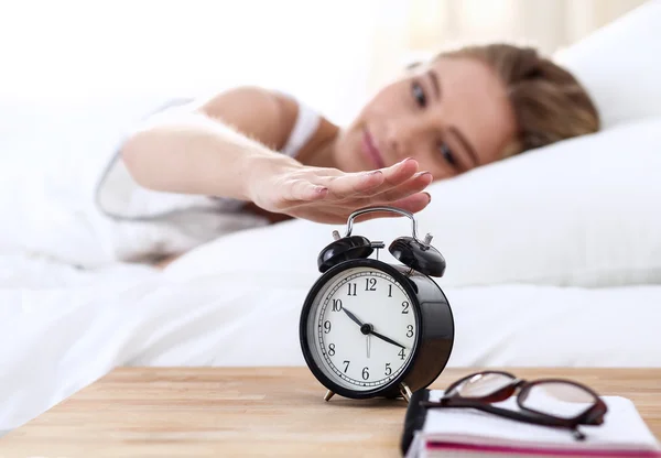 Young sleeping woman and alarm clock in bedroom at home