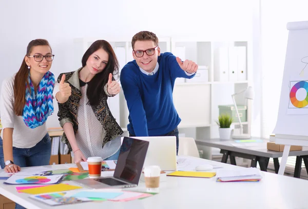 Young business people standing at office near desk and showing ok