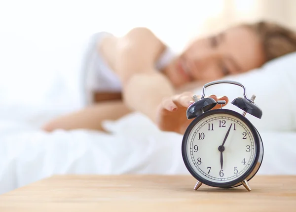 Young sleeping woman and alarm clock in bedroom at home