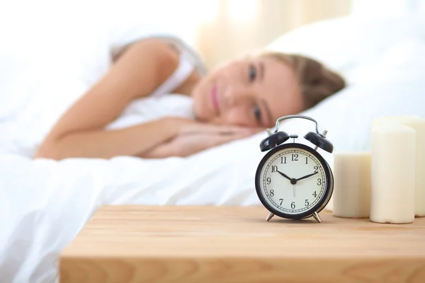 Young sleeping woman and alarm clock in bedroom at home