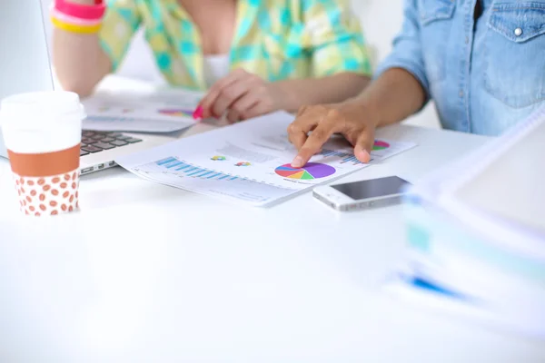 Two women working together at office, sitting on the desk