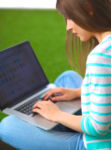 Young woman with laptop sitting on green grass