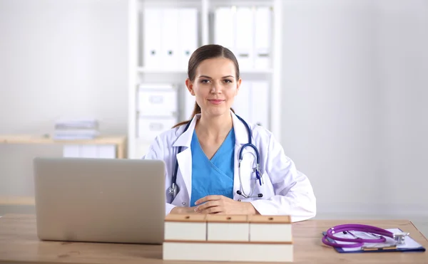 Beautiful young smiling female doctor sitting at the desk and writing.