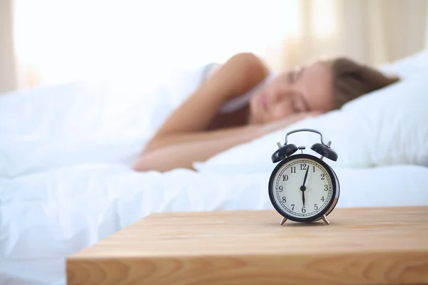 Young sleeping woman and alarm clock in bedroom at home