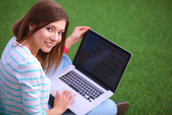 Young woman with laptop sitting on green grass