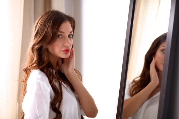 Young woman looking herself reflection in mirror at home