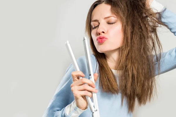 Funny woman with messy hair holding straightening irons