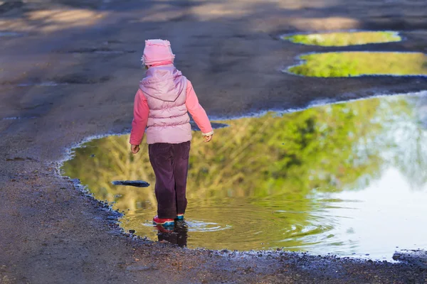 Back view of walking in spring puddle preschooler girl wearing purple nylon and pink bucket hat
