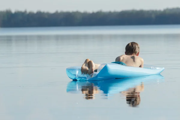 Back view of relaxed teenage boy floating on azure inflatable pool lounge outdoors