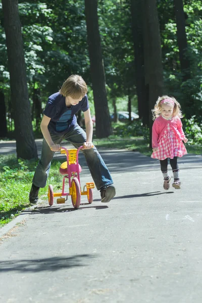 Sibling children playing tag game by running and riding kids tricycle