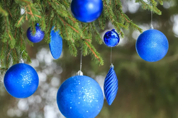 Outdoor Christmas ultramarine tinsel baubles hanging on snowy spruce twig