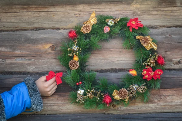 Human hand holding red bow and hanging on rustic log cabin wall with Christmas wreath