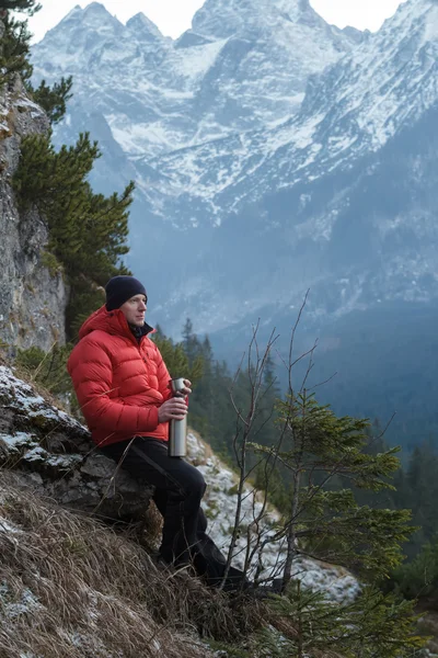 Resting mountain hiker with hot drink cup in hand at snowy winter mountains background