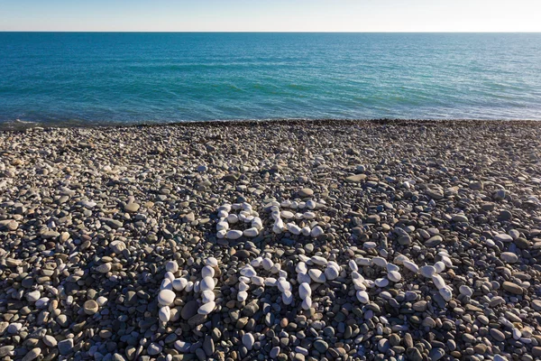 The sign be happy made from white pebbles on pebble beach on the sea