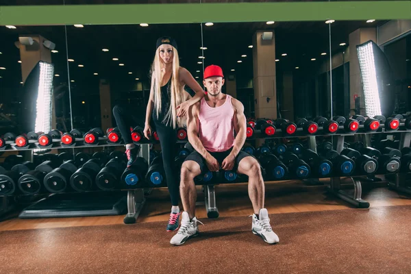 Sport, bodybuilding, weightlifting, lifestyle and people concept - Young beautiful couple in stylish clothes sitting a gym near the dumbbells