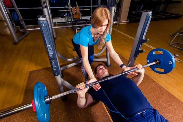 Personal trainer helping  men lift a barbell while working out in  gym