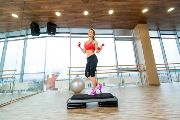 Girl performs step cardio with dumbbells in a gym