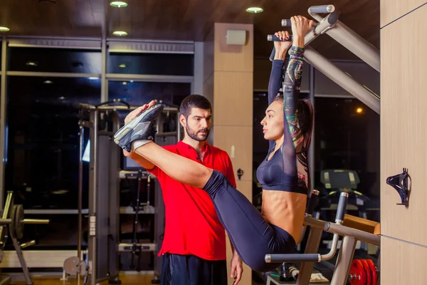 Fitness, sport, training and people concept - Personal trainer helping woman working with abdominal muscles press on the horizontal bar.