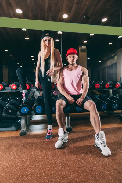Sport, bodybuilding, weightlifting, lifestyle and people concept - Young beautiful couple in stylish clothes sitting a gym near the dumbbells