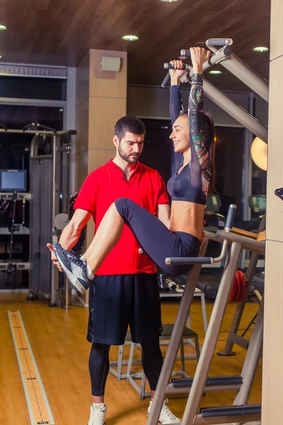 Fitness, sport, training and people concept - Personal trainer helping woman working with abdominal muscles press on the horizontal bar.