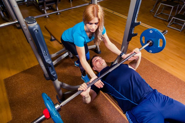 Personal trainer helping  men lift a barbell while working out in  gym