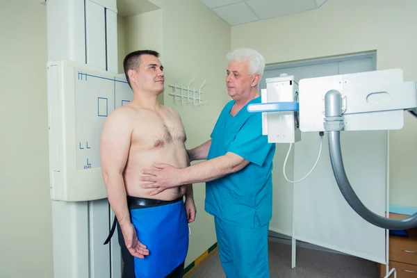 Mid adult man patient  mature male doctor setting up the machine to take x-ray