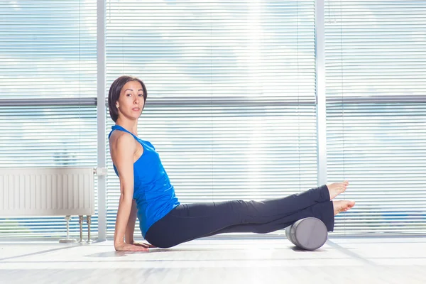Fitness, sport, training and lifestyle concept - woman doing pilates on the floor with foam roller