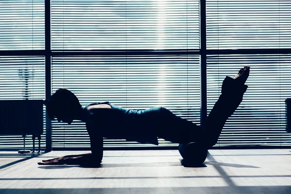 Fitness, sport, training and lifestyle concept - woman doing pilates on the floor with foam roller contour of the body against the window