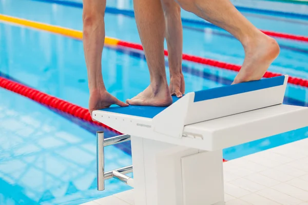 Young muscular swimmer in low position on starting block in a swimming pool