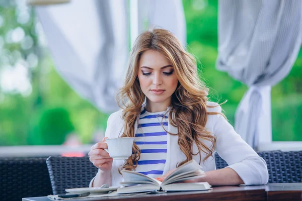 Beautiful young girl in outdoor cafe reading a book and drinking coffee. phone. student. business woman