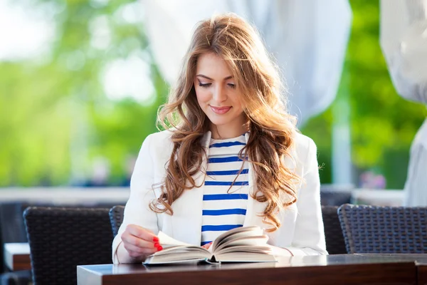 Beautiful young girl in outdoor cafe reading a book and drinking coffee. phone. student. business woman