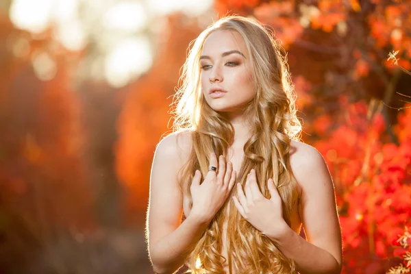 Young woman on a background of red and yellow autumn leaves with beautiful curly hair his chest, no clothes