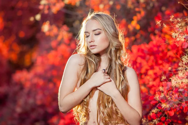 Young woman on a background of red and yellow autumn leaves with beautiful curly hair his chest, no clothes