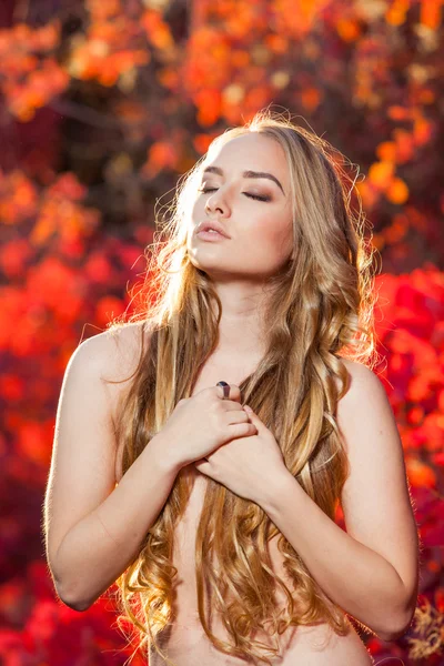 Young woman on a background of red and yellow autumn leaves with beautiful curly hair his chest, no clothes