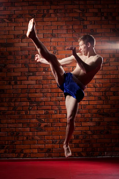 Muscular handsome fighter giving a forceful forward kick during  practise round with  boxing bag, kickboxing