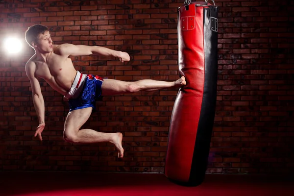 Muscular handsome fighter giving a forceful forward kick during  practise round with  boxing bag, kickboxing