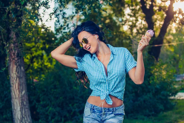 Young beautiful short blue hair hipster woman with headphones music in the park. ice cream