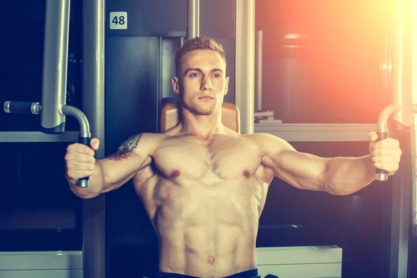 Brutal athletic man pumping up muscles on crossover
