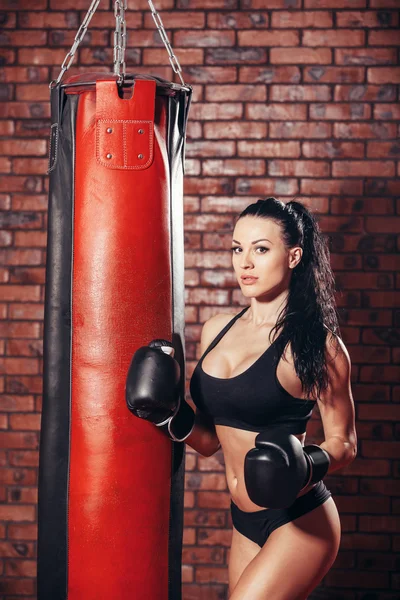 Young sexy girl with boxing gloves, punching bag, on the background wall of red brick.