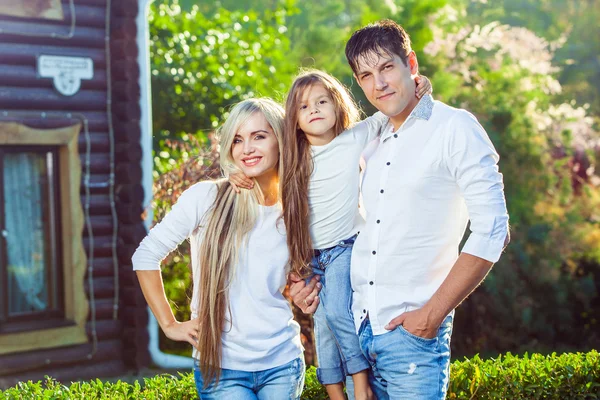 Happy family with child outdoors, against the background of a wooden house in jeans