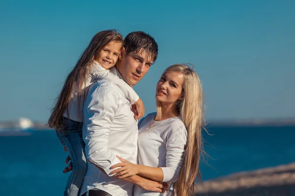 Young family in blue jeans hugging on the background of water