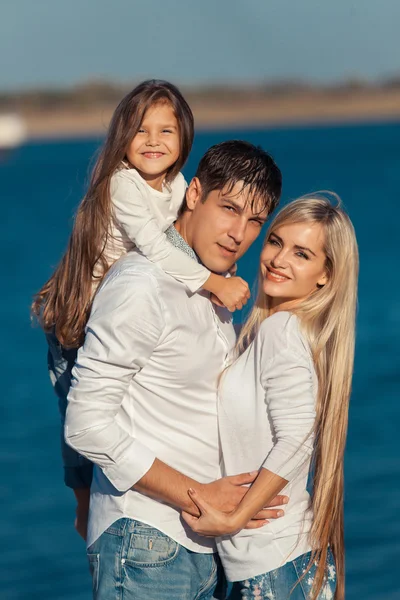 Young family in blue jeans hugging on the background of water