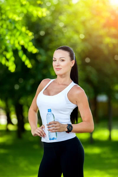 Woman athlete takes  break, she drinking water, out a run on  hot day