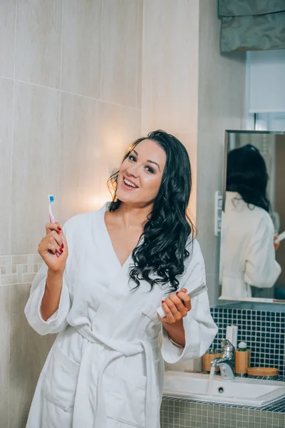 Portrait of attractive woman brushing teeth in bathroom  a white coat. healthy teeth.