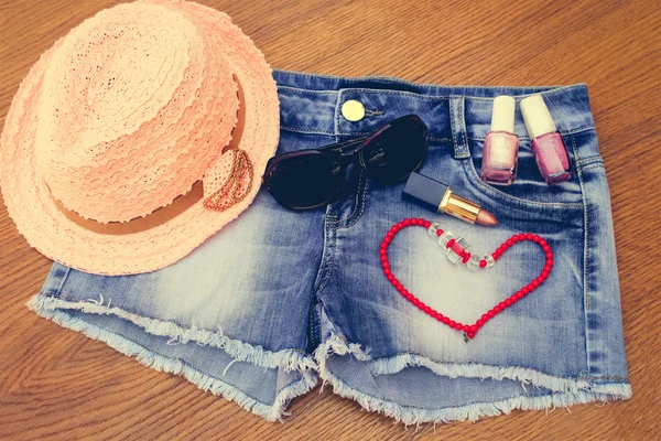 Summer women\'s accessories: red sunglasses , beads, denim shorts, sun hat, nail polish, lipstick open. Toned image.