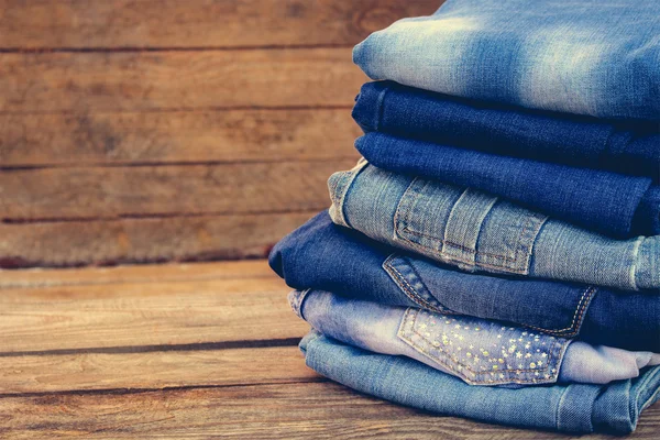 Pile of jeans clothes on wooden background. Toned image.